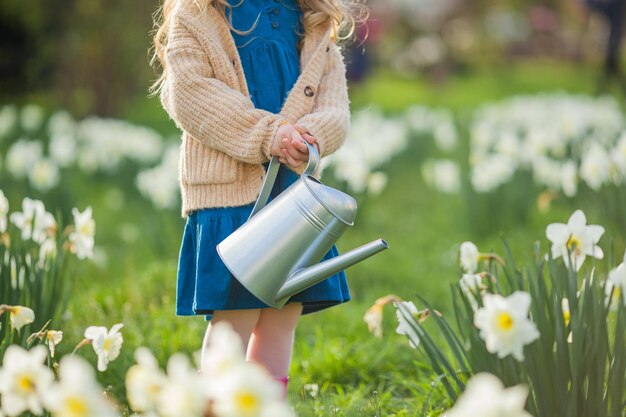 Pasen Schattig klein meisje van 5 jaar oud met konijnenoren geeft narcissen water op het gazon Gelukkig kind Lentevakantie