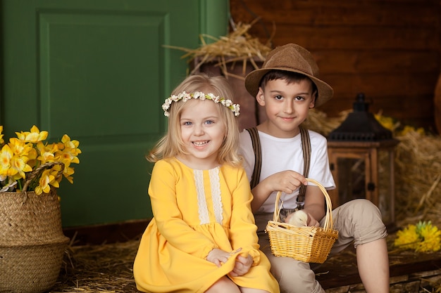 Pasen! Schattige kleine gelukkige kinderen, een jongen en een meisje in het hooi met dieren - kippen en een konijn op Paasdag. Kinderen hebben plezier, spelen en knuffelen.