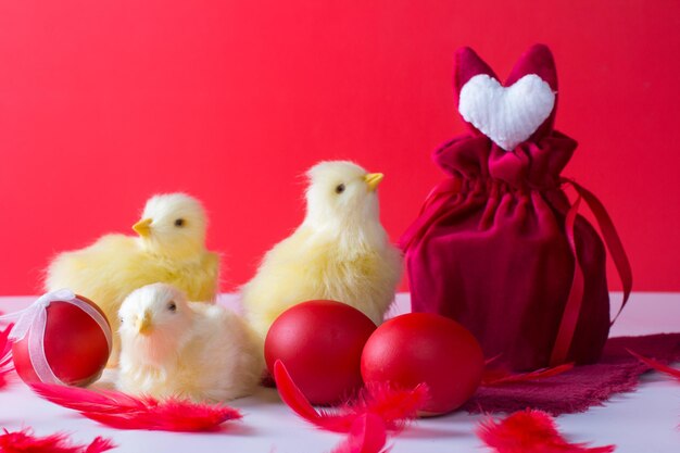 Pasen stilleven met een wit konijn en kippen op een rode achtergrond Een glas wijn en beschilderde eieren het concept van de heldere paasvakantie