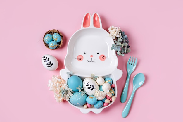 Pasen tafeldecoratie decoratie met schattige plaat in de vorm van een konijntje met paaseieren en snoep op roze achtergrond Happy Easter concept Idee voor paasdiner