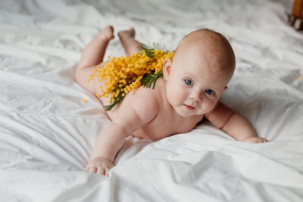 Pasgeboren baby bedekt met een takje mimosa ligt op zijn buik op een wit bed, gelukkig zorgeloos