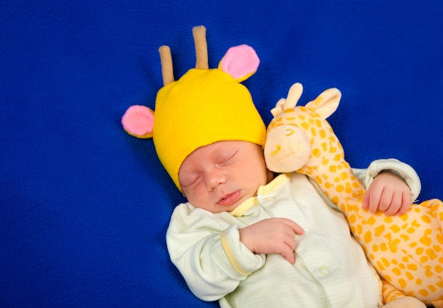 Pasgeboren baby die op een blauwe deken met stuk speelgoed giraf ligt. Jongen of meisje