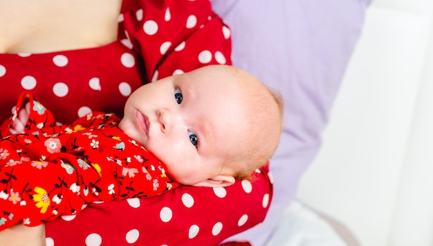 Pasgeboren baby meisje op de handen van de moeder in een rode polka dot jurk
