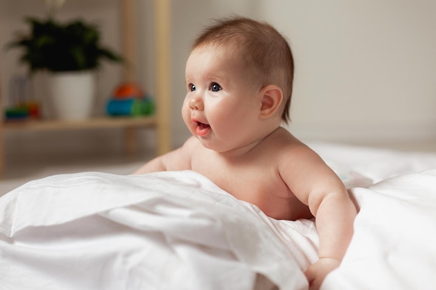 Pasgeboren baby met ontbloot bovenlichaam ligt op zijn buik op een bed met wit beddengoed