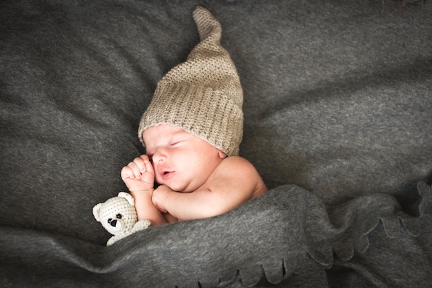 Pasgeboren baby slaapt met een speeltje naast de gebreide teddybeer