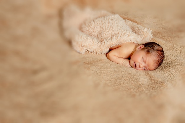 Pasgeboren baby slaapt, rustend op haar eigen handen en ellebogen, op bruine achtergrond.