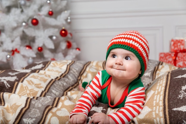 Pasgeboren babyjongen gekleed in kabouterkostuum liggend op wit bonttapijt tussen kerstversieringen