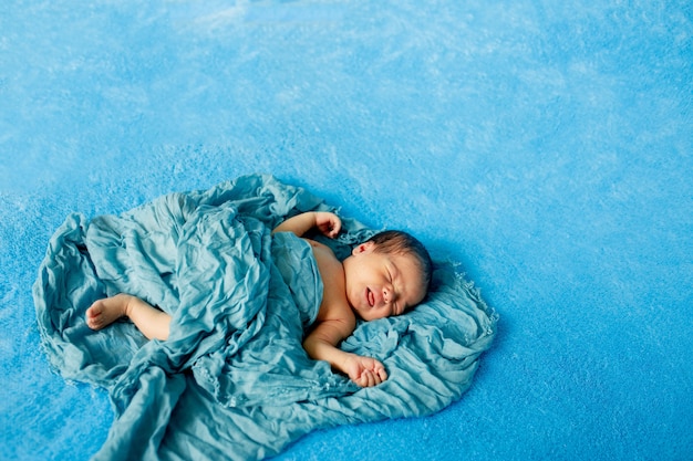 Pasgeboren babyjongen liggend op zijn rug ontspannen onder een blauwe omslagdoek