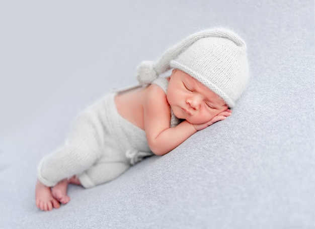 Pasgeboren babyjongen met een gebreide broek en muts die slaapt en kleine handjes onder zijn wangen houdt. schattig baby kind dutten in studio