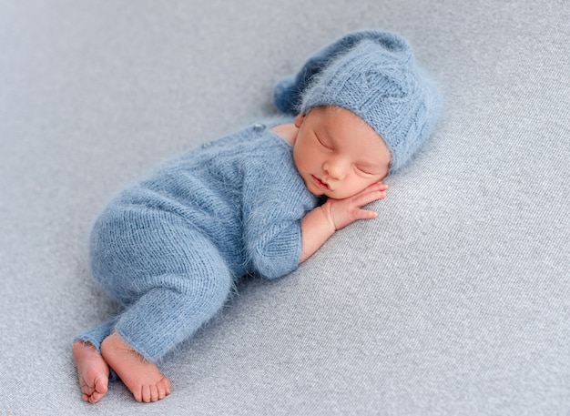 Pasgeboren babyjongen met gebreid kostuum en sokken die op kussen slapen en kleine handen onder zijn wangen houden. Schattig baby kind dutten