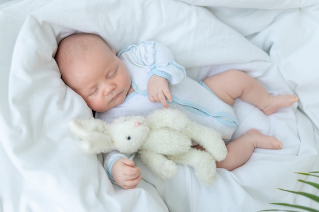 Pasgeboren babyjongen slaapt zeven dagen in een wieg thuis op een katoenen bed met een speeltje in zijn hand, close-up.