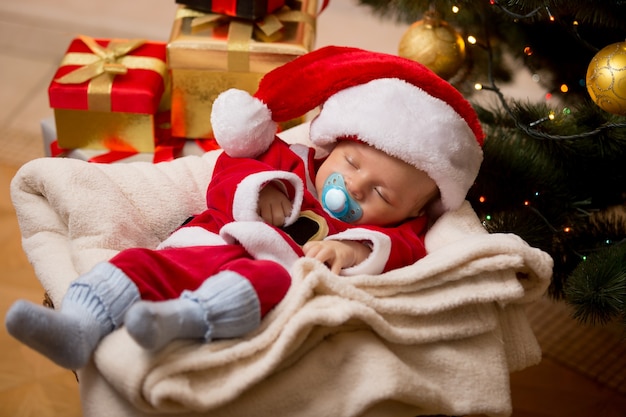 Pasgeboren babyjongen slapen in de woonkamer bij de kerstboom en dozen met cadeautjes