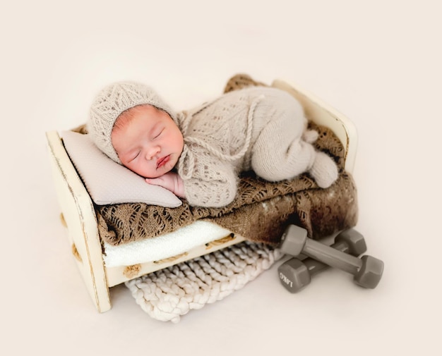 Pasgeboren babyjongen slapen met gebreid beige kostuum op handgemaakt ontworpen bed. Baby kind kind dut tijdens studio fotoshoot