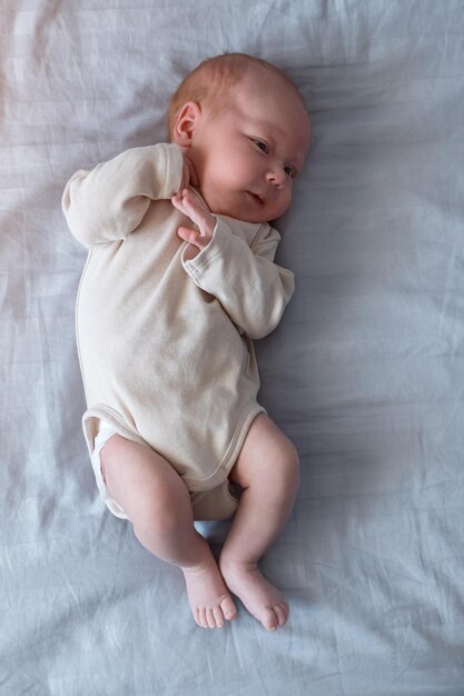 Pasgeboren babymeisje in beige bodysuit ligt op bed in de kamer