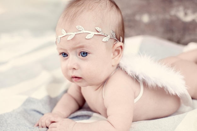 Foto pasgeboren babymeisje met blauwe ogen een lauwerkrans in haar haar en engelenwinden