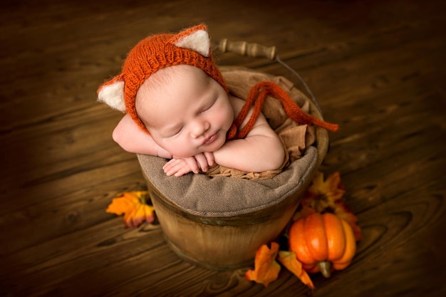 Pasgeboren babymeisje slapen op de achtergrond van natuurlijk bruin hout in een houten emmer Een pasgeboren baby met een roodbruine tijgerwelpje op zijn hoofd Mooi portret van een pasgeboren baby met rode pompoenen