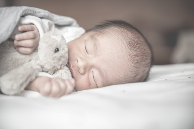 Pasgeboren babyslaap op bed met weinig konijn. Familie en liefdeconcept. Aziatisch jong geitje.