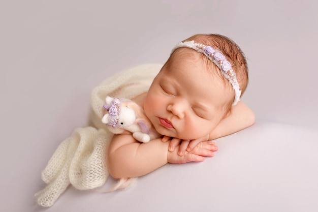 Pasgeboren meisje slapen in de eerste dagen van het leven op een witte achtergrond Close-up studio portret van een kind Een pasgeboren baby is gewikkeld in een witte gebreide deken met een witte hoofdband