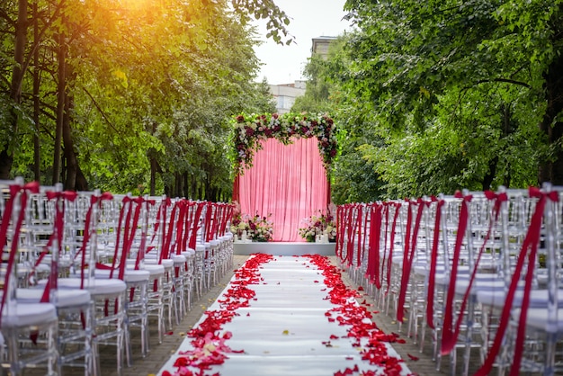 バラの花びらで飾られた椅子の間の通路は、結婚式のアーチにつながります