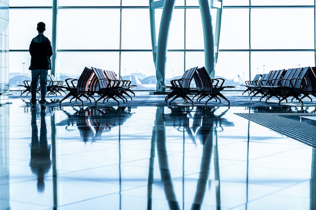 Passagier die zich in een lobbyluchthaven bevindt die op vlucht in silhouet wacht