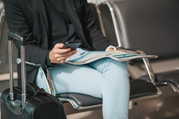 Passagier in een luchthavenlounge die wacht op vluchtvliegtuigen jonge man met smartphone in luchthaven wacht
