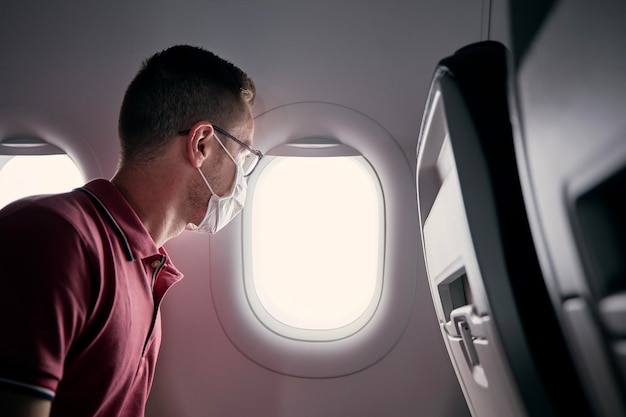 Passagier met een beschermend gezichtsmasker in het vliegtuig die door het raam kijkt