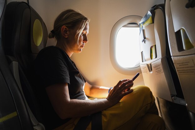 Passagier vrouw vliegt in een vliegtuig meisje met behulp van de telefoon zitten bij het vliegtuig raam reizen vrouw met