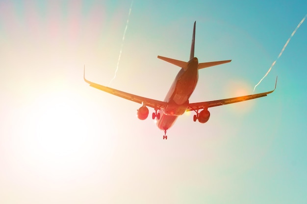 Passenger airplane flies near the sun glare with a color rainbow gradient on landing, with the wings of a steam jet vortex.