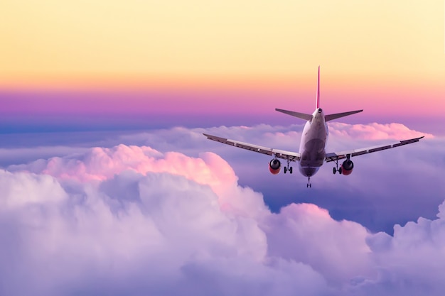 Passenger airplane landing against amazing yellow and pink colorful sky with clouds during sunset.