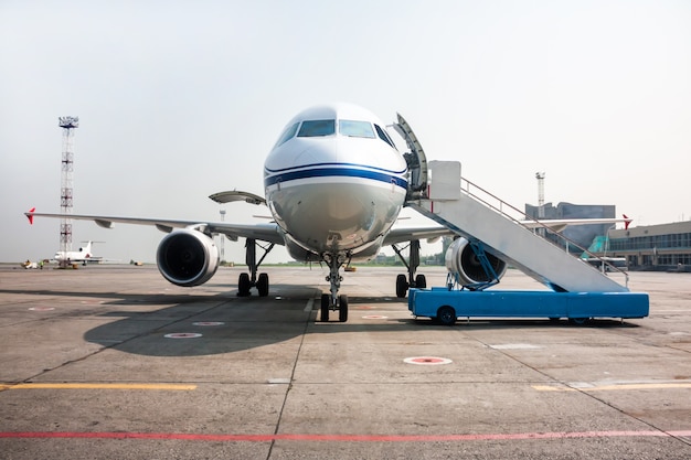 Пассажирский самолет с открытым багажным отделением и посадочной рампой возле перрона аэропорта