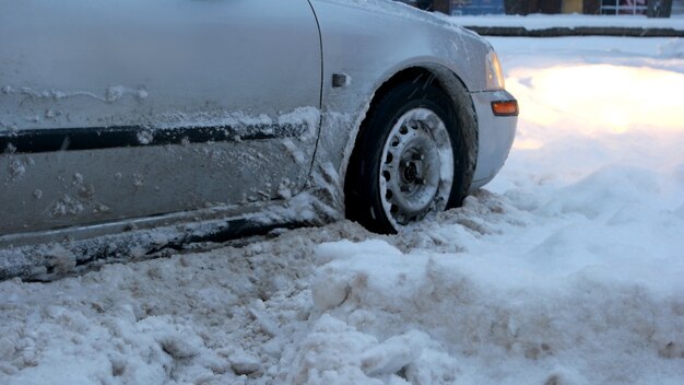 Легковой автомобиль заглох на заснеженной дороге. Автомобиль застрял в снегу после сильной метели, кадрированное изображение. Плохие погодные условия.