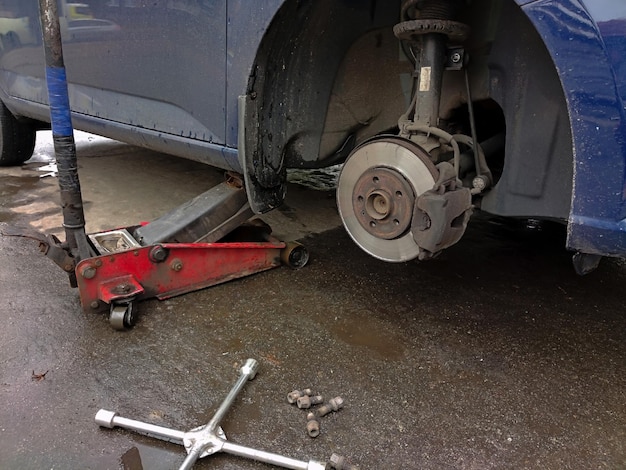 A passenger car with the front wheel removed is lifted on a towing jack Nuts  wrench are scattered