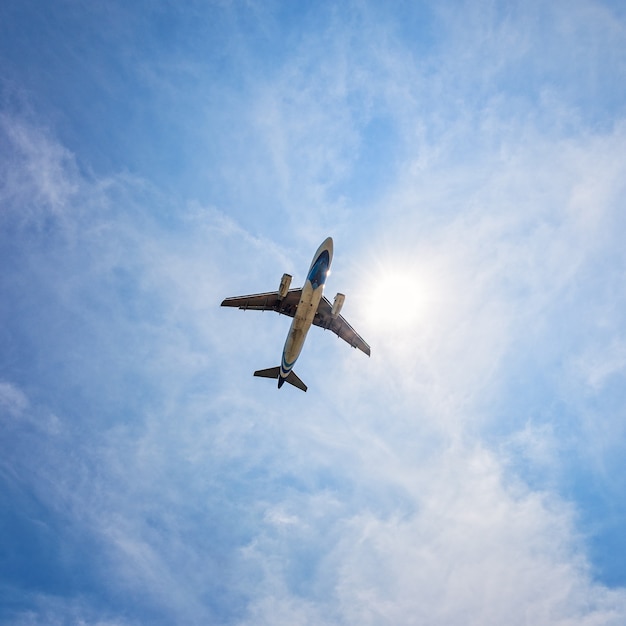 Foto sotto l'aereo a reazione del passeggero che vola attraverso il sole nel cielo azzurro e nelle nuvole