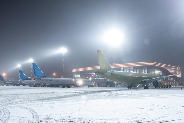 사진 눈이 내린 겨울 밤 에 터미널 에 있는 공항 기지 에 있는 여객 항공기