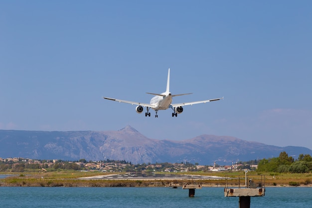 Passenger's airplane is landing at Kerkyra Airport. Greece, Corfu island. Decrease in height, close-up. Runway on the background of mountains and sea.