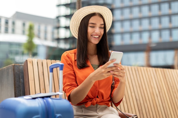 스마트폰으로 문자 메시지를 보내고 온라인으로 티켓을 예약하는 승객 여성이 야외에 앉아 있습니다.