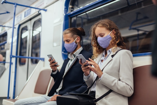地下鉄車両に座ってスマートフォンを使用して保護マスクを着用している乗客。健康保護の概念。