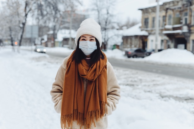 Passerby Asian woman in a protective medical mask outdoors. A woman on the street in winter protects the respiratory tract from the epidemic of coronavirus.