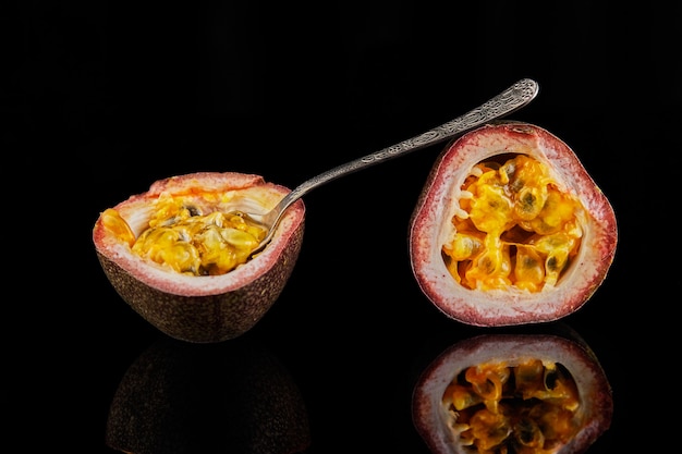 Passiflora is cut into two halves with a spoon inside isolated on a black surface