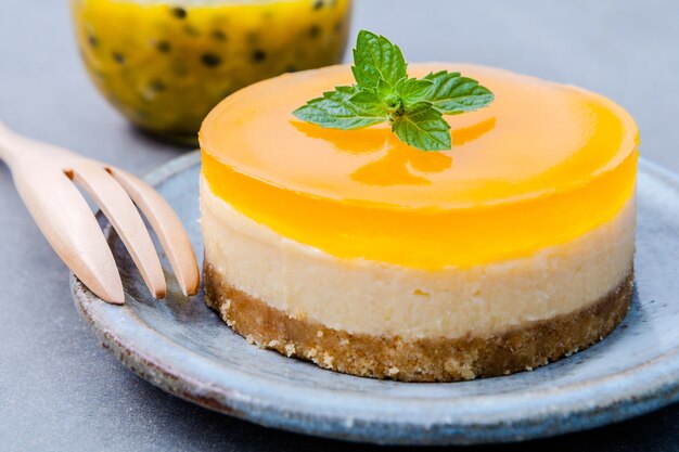 Cheesecake frutto della passione con foglie di menta fresca su sfondo scuro.