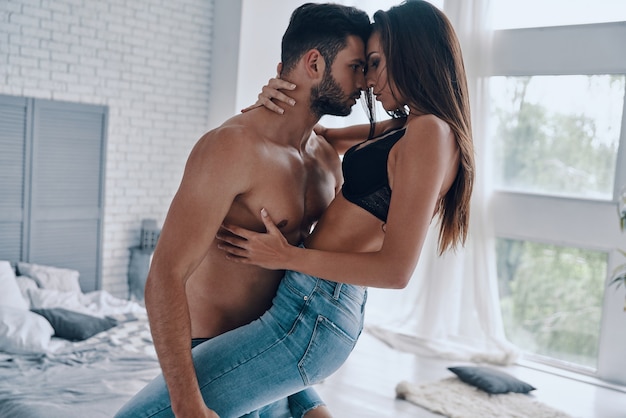 Passion. Handsome young shirtless man carrying semi-dressed attractive woman while standing in the bedroom