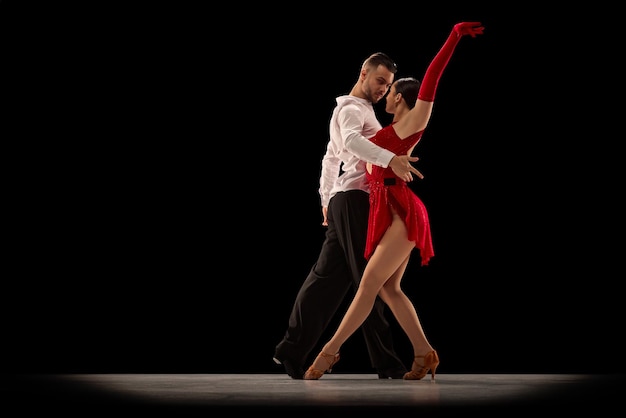 Passionate attractive young man and woman professional ballroom dancers dancing tango over black