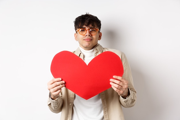 Photo passionate man waiting for lover with big red heart on valentines day, looking romantic and with love, standing over white background.