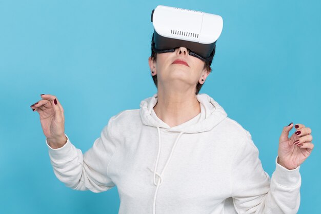 Passionate middle-aged woman in sweater is watching new film with glasses of virtual reality on red-blue wall. Concept of high technology accessibility for middle-aged people. 