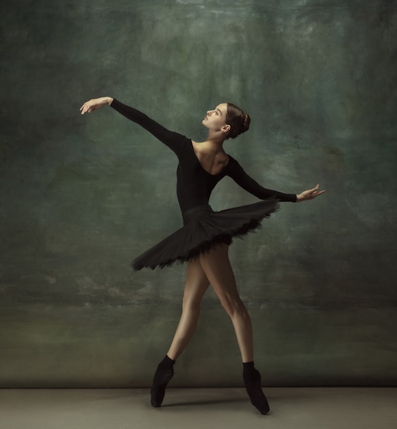 Passioned. Graceful classic ballerina dancing, posing isolated on dark studio background. Elegance black tutu. Grace, movement, action and motion concept. Looks weightless, flexible. Fashionable.