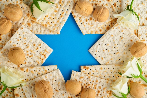 Passover celebration concept Blue Star of David made from matzah white and yellow roses kippah and walnut on bluebackground Traditional ritual Jewish Passover food Pesach Jewish holiday Mock up