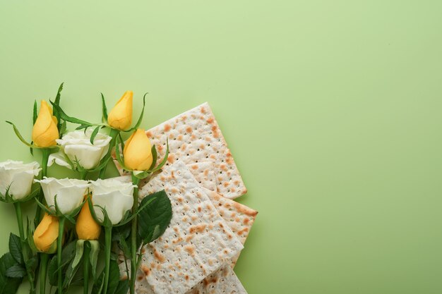 Passover celebration concept Matzah kosher red wine walnut and spring white and yellow rose flowers Traditional ritual Jewish bread on light green background Passover food Pesach Jewish holiday
