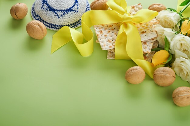 Passover celebration concept Matzah kosher red wine walnut and spring white and yellow rose flowers Traditional ritual Jewish bread on light green background Passover food Pesach Jewish holiday