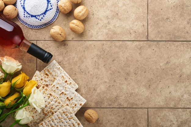 Photo passover celebration concept matzah kosher red wine walnut and white and yellow roses traditional ritual jewish bread on sand color old tile wall background passover food pesach jewish holiday