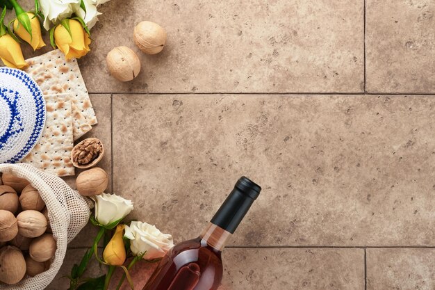 Passover celebration concept Matzah kosher red wine walnut and white and yellow roses Traditional ritual Jewish bread on sand color old tile wall background Passover food Pesach Jewish holiday